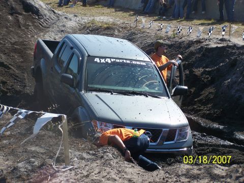 1989 Ford Bronco - A pickup truck is stuck in a mud pit during an off-road event, with spectators watching.