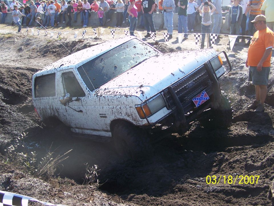 white SUV stuck in mud pit with people watching