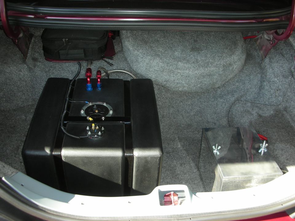 Trunk with large black fuel cell, red and blue fittings, and spare tire well