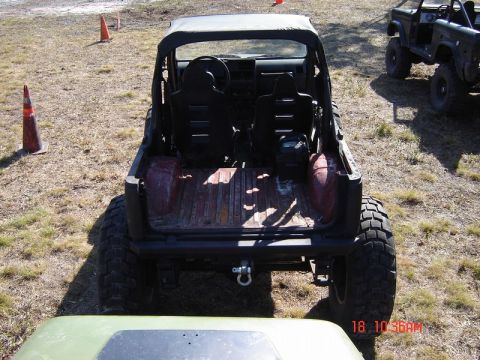 1989 Ford Bronco - This lifted off-road vehicle, seen from the rear, has a soft top and large tires. Another similar vehicle is parked in the background.