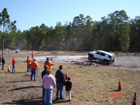 1989 Ford Bronco - Toyota FJ Cruiser jumps during an off-road event with spectators observing.