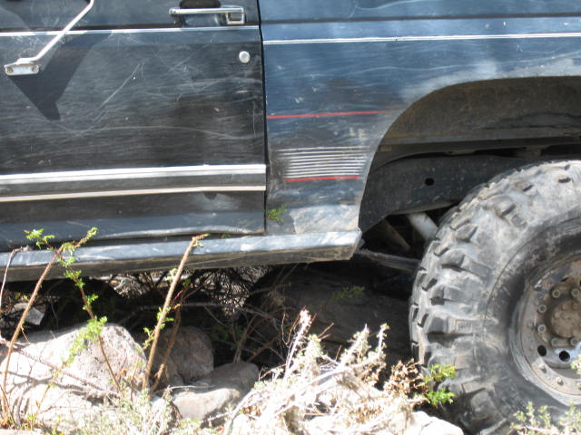 Side view of a dark-colored off-road vehicle with large tires, parked on rocky terrain