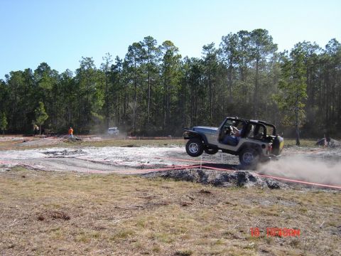 1989 Ford Bronco - A Jeep Wrangler jumps over a dirt obstacle during an off-road event.