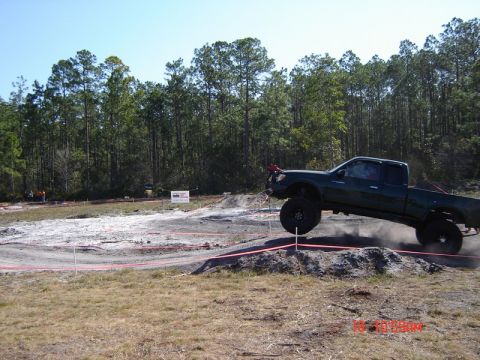 1989 Ford Bronco - A modified pickup truck navigates a challenging off-road course, with one wheel in the air.