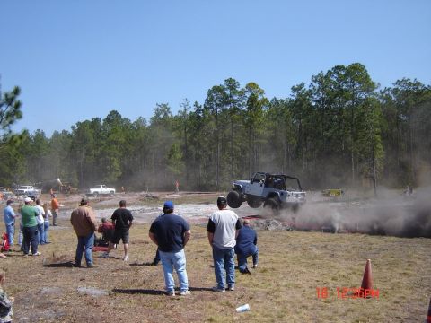 1989 Ford Bronco - A Jeep Wrangler performs a jump at an off-road event, with spectators observing the action.