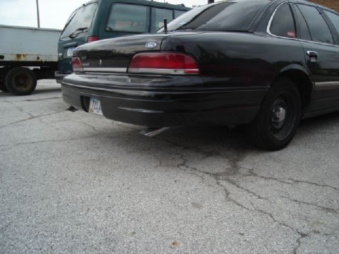 1992 Ford Crown Victoria - The rear of a black 1992 Ford Crown Victoria is visible, parked next to other vehicles.