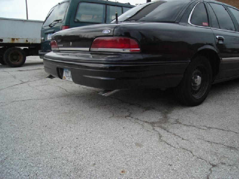Black 1992 Ford Crown Victoria sedan, rear view, parked on asphalt with a trailer and green van nearby