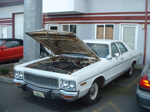 2000 Ford Crown Victoria - This white sedan, likely a 1975 model, is parked with its hood open, revealing the engine compartment.