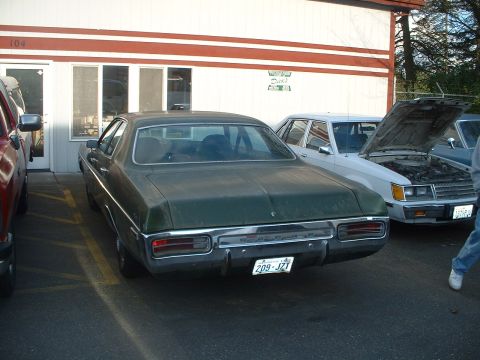 2000 Ford Crown Victoria - A green sedan is parked in front of a building with a white car next to it, which has its hood open.
