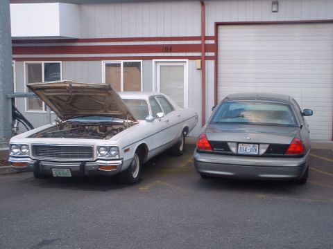 2000 Ford Crown Victoria - Two sedans, one with its hood open, are parked in front of a building with a large garage door.