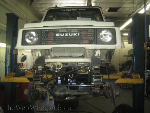 1987 Suzuki Samurai - Front view of a Suzuki Samurai undergoing suspension modifications in a garage.