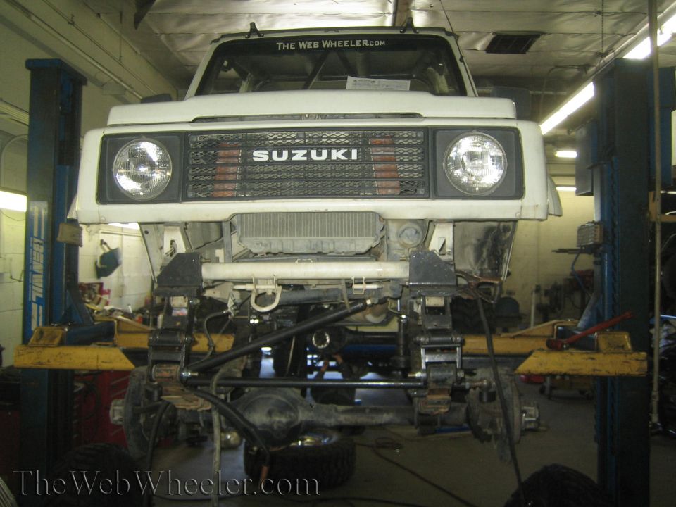 Suzuki Samurai on lift, front end disassembled for suspension work. The Web Wheeler logo visible