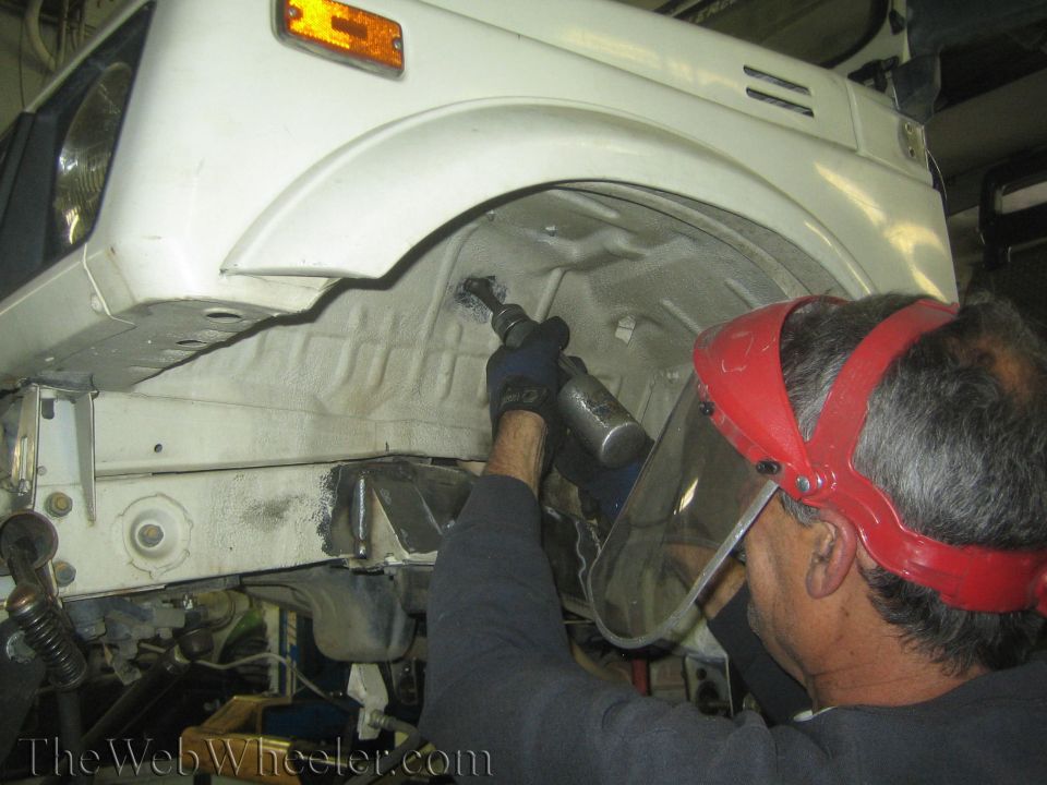 White Suzuki Samurai wheel well being worked on by a person wearing a face shield and gloves