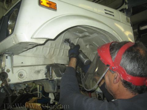 1987 Suzuki Samurai - A person is using a tool to work on the interior of a vehicle's wheel well.