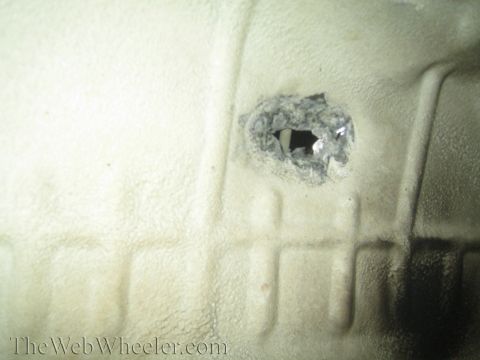 1987 Suzuki Samurai - A hole is visible in a textured panel, showing damage and an opening to darkness beyond.