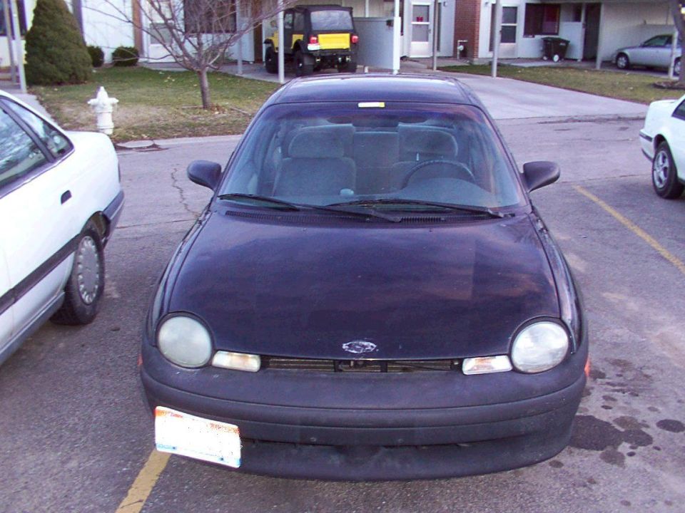 dark sedan parked in lot, white car to left, yellow jeep and other cars in background