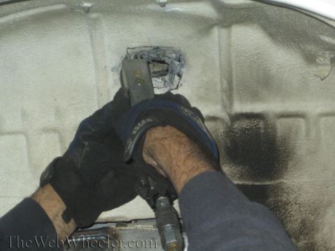 1987 Suzuki Samurai - Hands work on a vehicle's frame, modifying a shock mount.