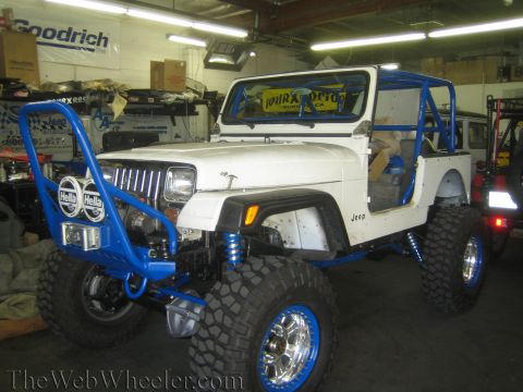 1987 Suzuki Samurai - Modified white Jeep Wrangler with custom blue roll cage and off-road tires.
