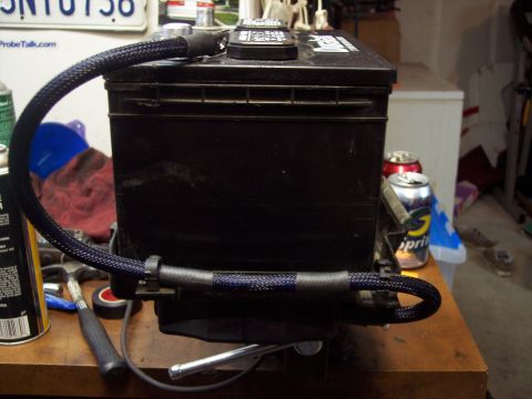 1995 Ford Probe - A car battery is mounted in a vise on a workbench, with braided cables connected to its terminals.