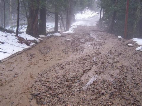 1966 Land Rover Discovery - A muddy forest road is covered in gravel and snow, with water flowing down its center.