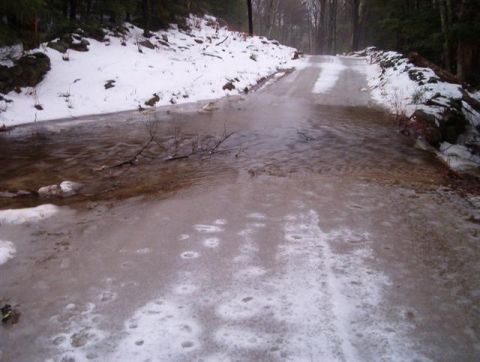 1966 Land Rover Discovery - A dirt road is flooded and partially frozen over, with snow lining the sides and trees in the background.