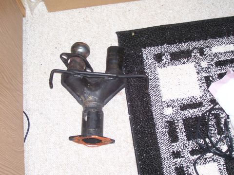 1993 Mazda MX-6 - An exhaust manifold part is shown on a carpeted floor next to a black and white patterned rug.