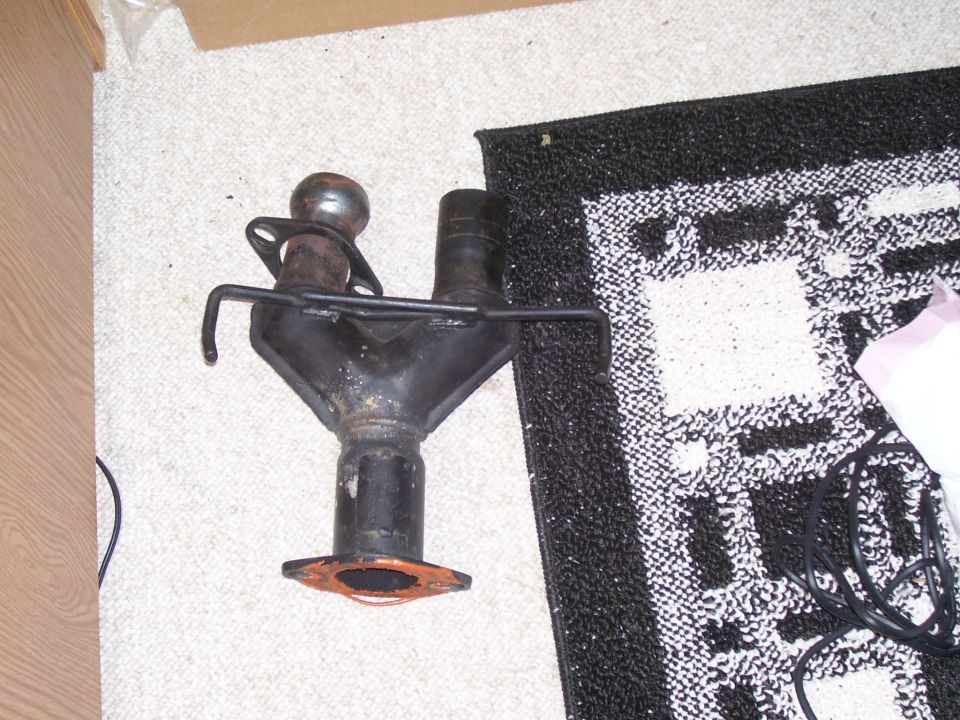 Black metal exhaust manifold with two pipes merging into one, resting on a carpet
