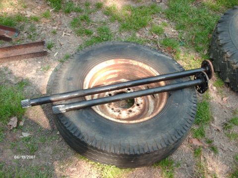 1990 Ford F-150 - Two axle shafts are laid across a tire, with other tires and metal pieces visible in the background.