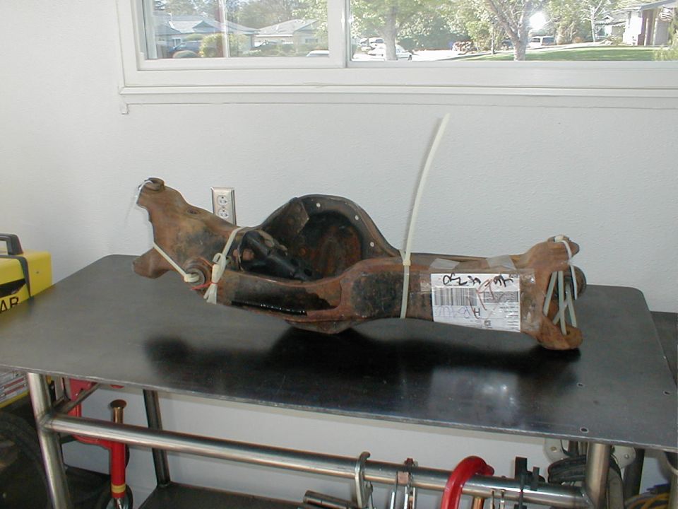 Rusty bare front axle housing with zip ties and shipping label on a black metal shop table