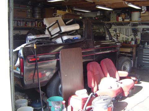 1978 Ford Bronco - A 1978 Ford Bronco sits in a cluttered garage, filled with various items including seats and a table.