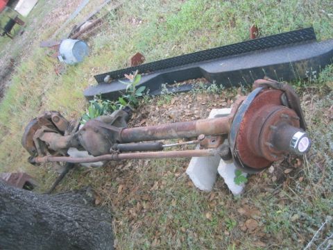 1973 Ford F-100 - A rusty truck rear axle assembly is shown outdoors, with a black metal object and vegetation in the background.