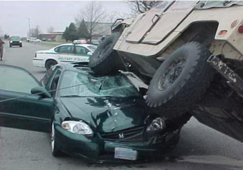1986 Ford LTD Crown Victoria - A military vehicle has landed on top of a car after a collision, with a police car nearby.