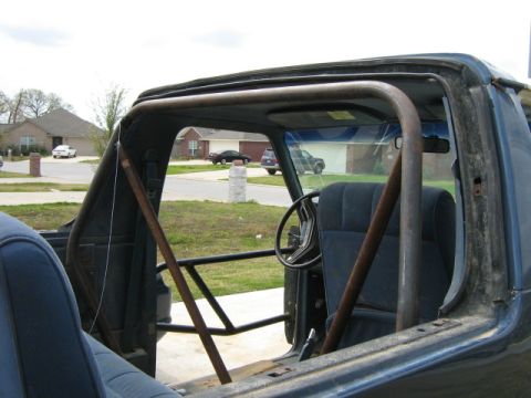 1986 Ford Bronco - The interior of a vehicle is visible, a custom roll cage and dark blue upholstery.