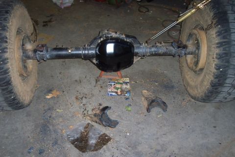 1994 Ford F-150 - A rear axle assembly with tires is shown, with detached suspension components scattered on the ground.
