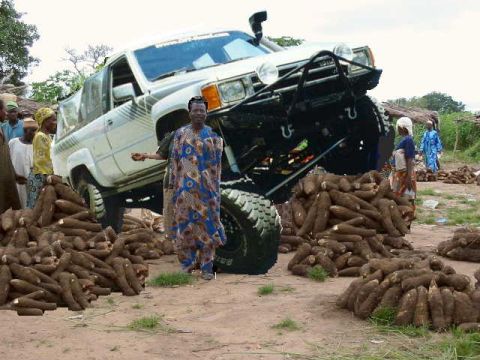 1979 Ford Bronco - A heavily modified Toyota pickup truck is displayed with piles of root vegetables and several people nearby.