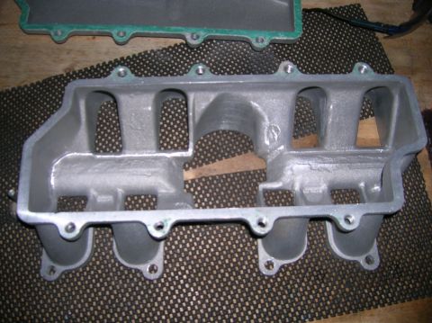 1998 Ford Crown Victoria - underside of a cast-aluminum intake manifold sits on a black perforated rubber mat with a green gasket nearby.