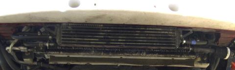 1997 Ford Taurus - Low-angle view under the front bumper of a white car showing an auxiliary transmission fluid cooler mounted ahead of the radiator, with bra…