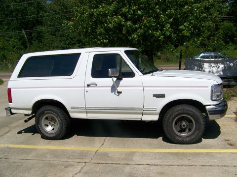 1995 Ford Bronco - This white 1995 Ford Bronco is shown from the side, parked outdoors with a wooded area behind it.
