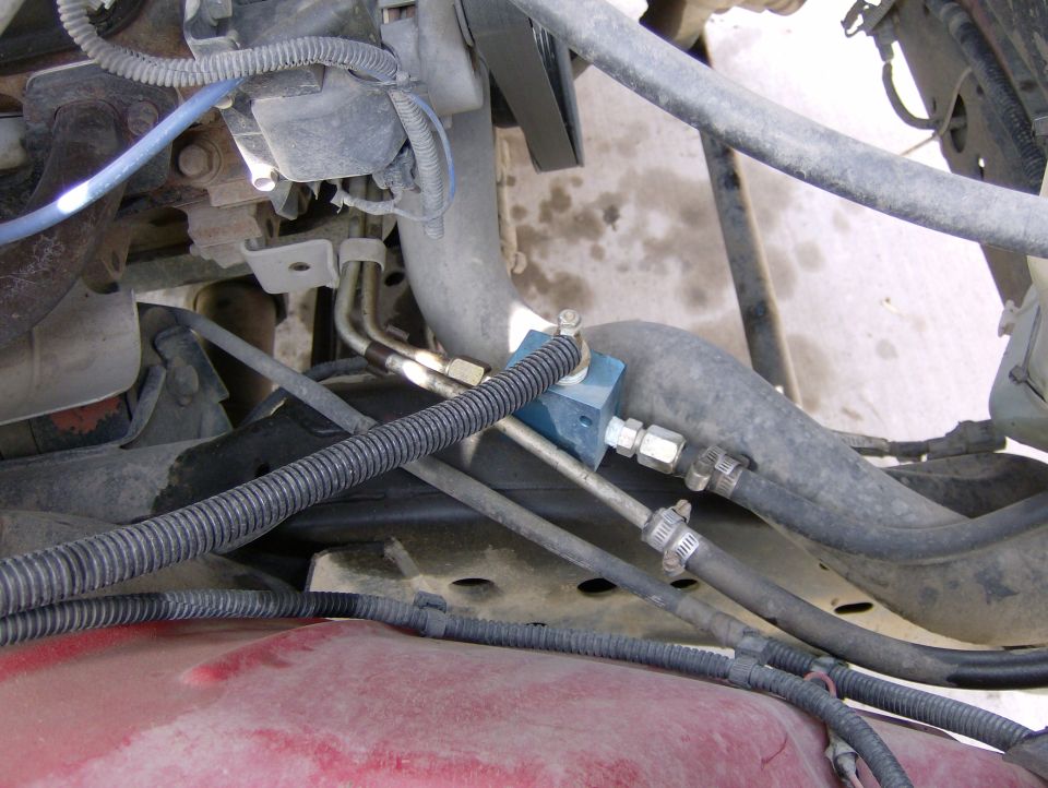 Engine compartment with hoses, wires, and a blue valve. Red painted metal is visible at the bottom