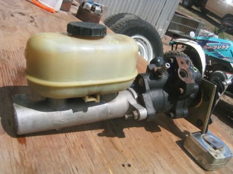 1973 Ford F-100 - A used hydro-boost brake booster bolted to an aluminum tandem master cylinder with a translucent plastic reservoir and black cap, resting o…