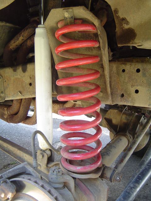 1978 Ford Bronco - Vehicle suspension detail showing a red coil spring and white shock absorber.
