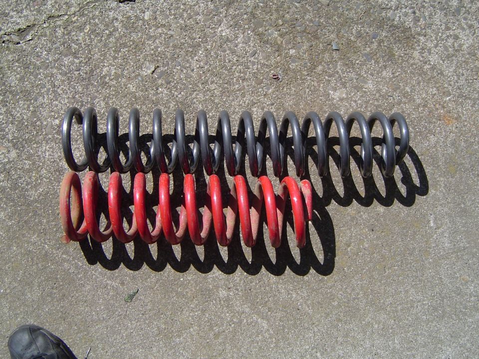 Long black coil spring next to shorter red coil spring lying on concrete