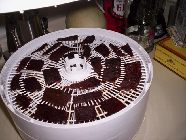 Food dehydrator filled with strips of jerky on its drying racks