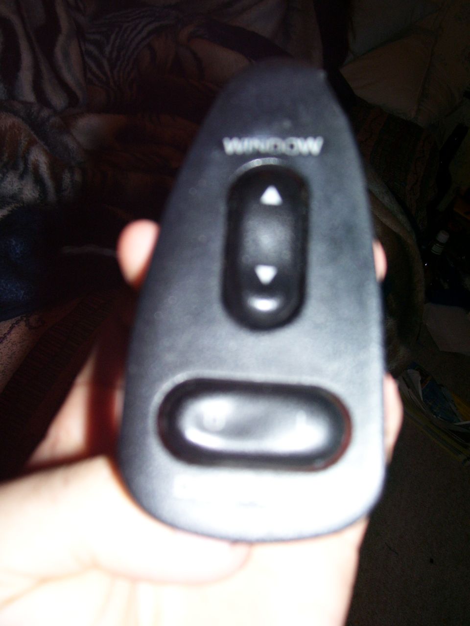 Hand holding a black power window switch with up and down arrows and a lock button. Text reads 'WINDOW'