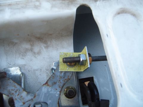 1997 Ford Ranger - Detail of a vehicle's tailgate latch assembly, showing a bolt securing a yellow bracket to a metal rod.