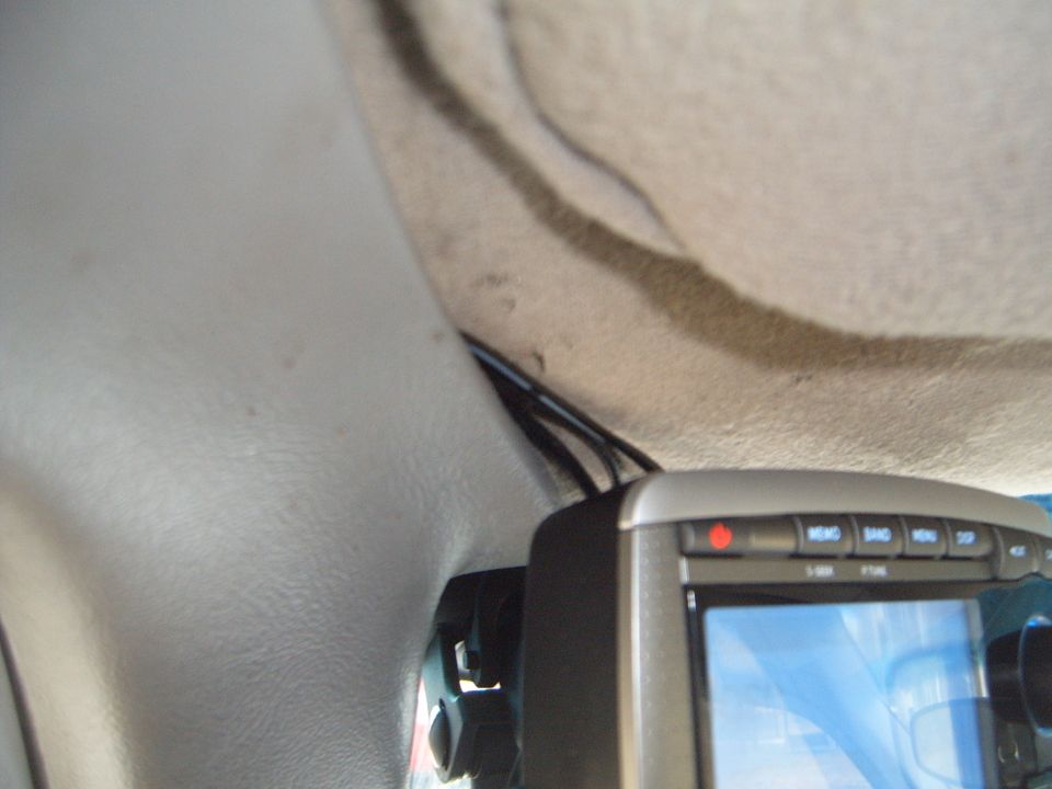 Close-up of a car's interior showing a GPS device mounted near the headliner, with wires visible