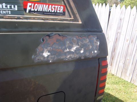 1988 Ford Bronco - Rear quarter panel of a dark SUV shows significant rust damage, with a Flowmaster sticker visible above.