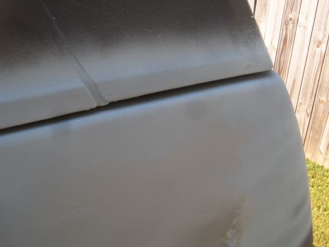 1988 Ford Bronco - A close-up view of a vehicle's body panel, possibly undergoing repair or painting, with a wooden fence visible in the background.
