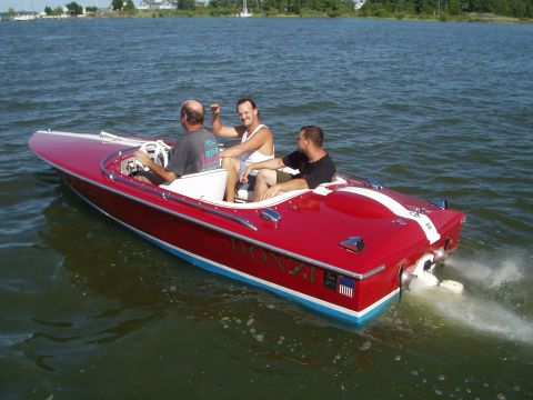 1978 Ford F-250 - A red Donzi boat with three men cruises on the water, showing its rear profile and outboard motor.