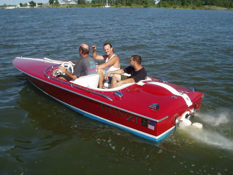 Red boat with white stripe, 'DONZI' visible on side, three men aboard, moving on water